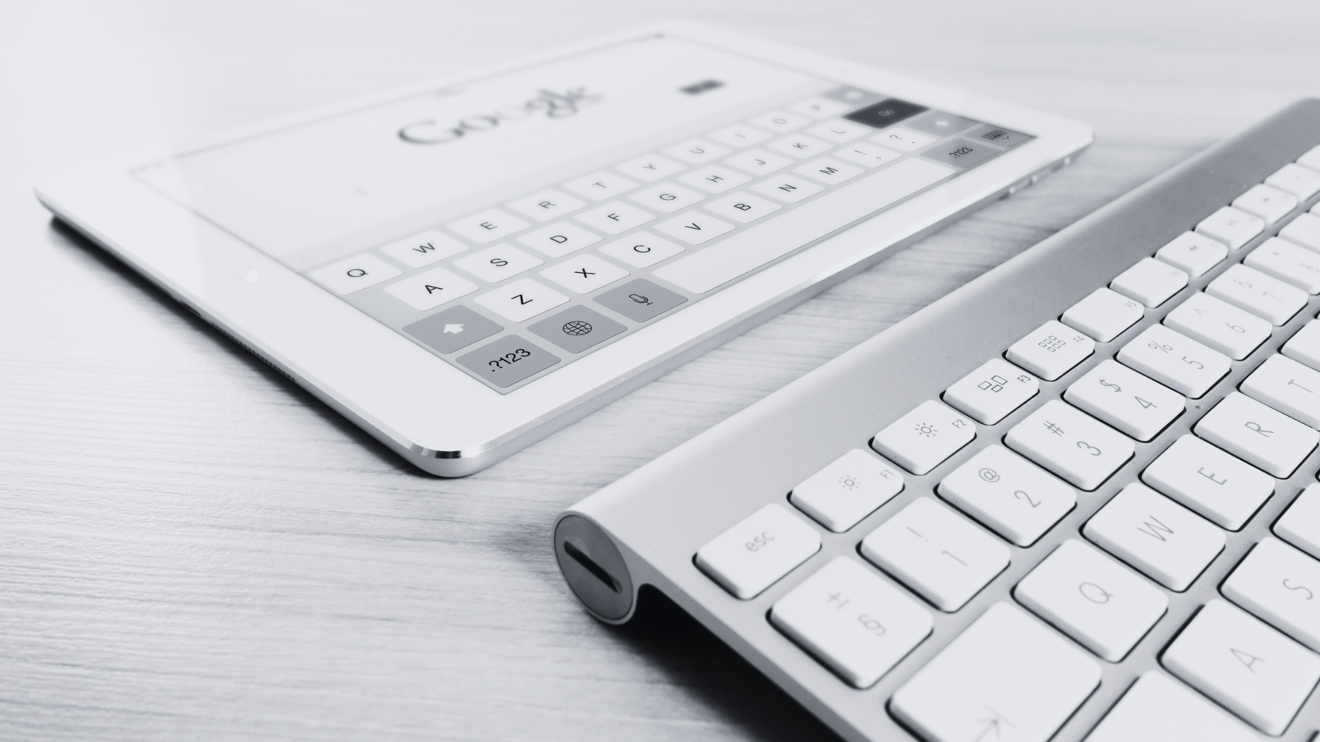 Close-up view of a sleek tablet displaying a Google search screen, paired with a modern wireless keyboard on a clean wooden surface.