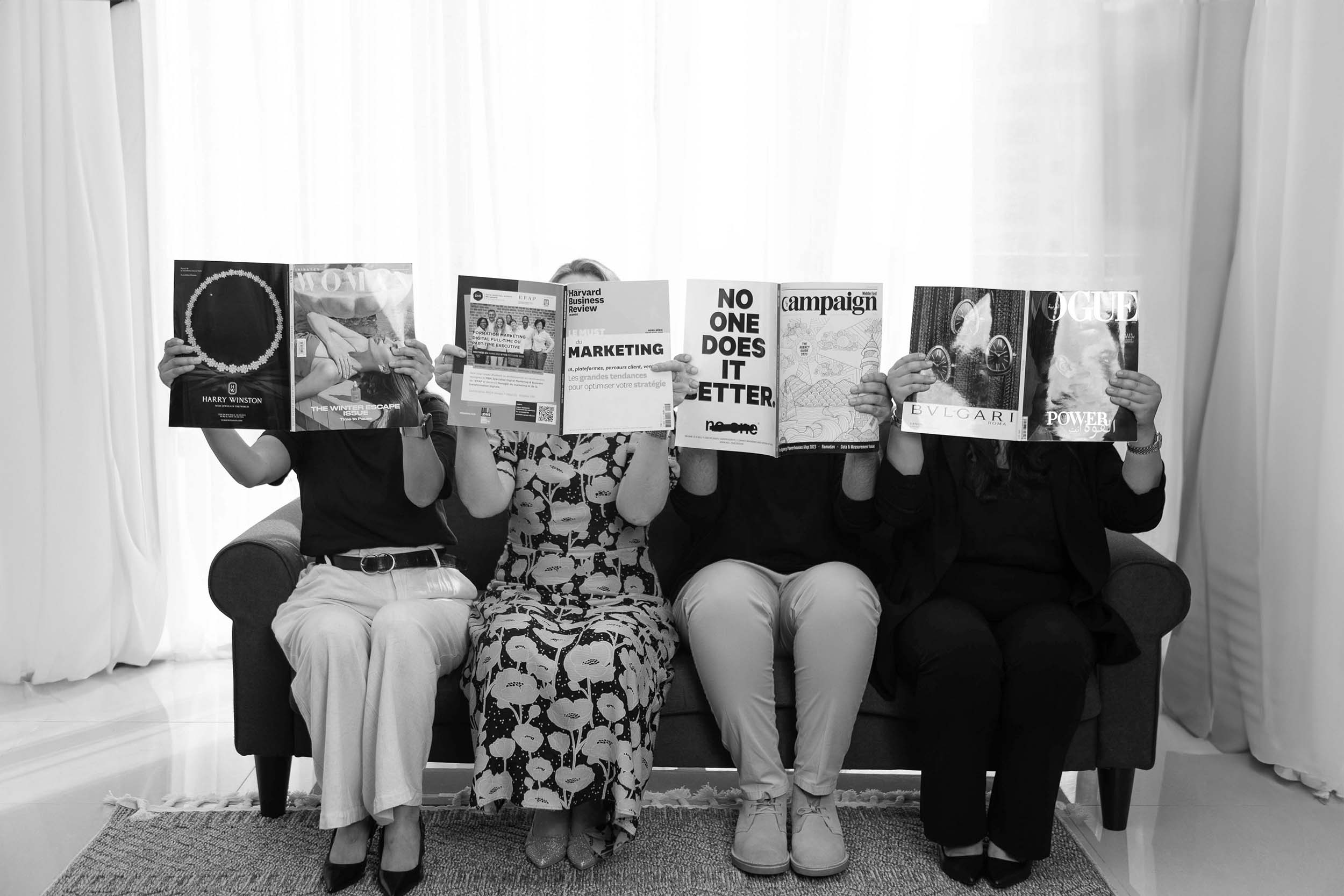 A creative scene of individuals seated on a couch, each holding a magazine to their face, showcasing diverse themes and perspectives in a lively, artistic setup.