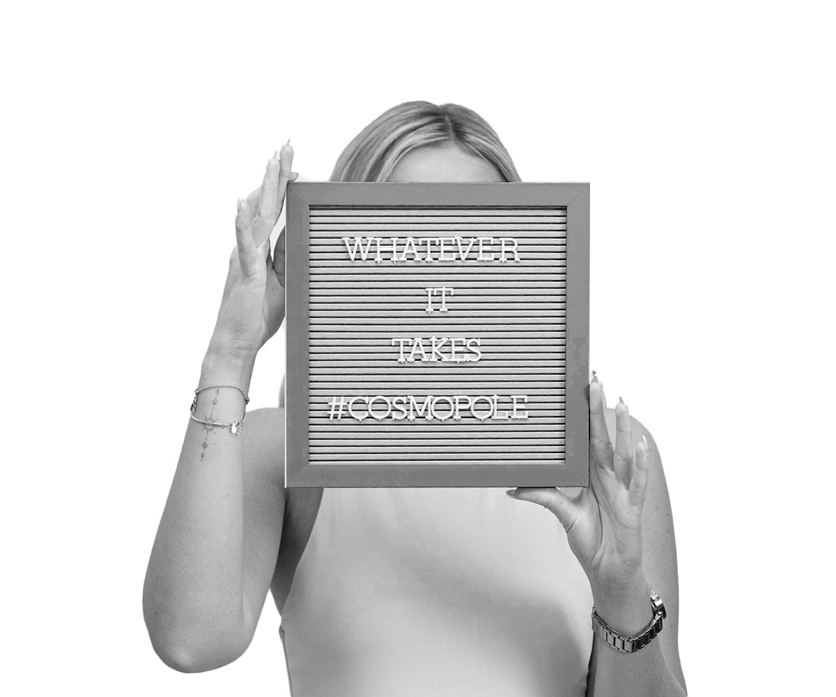 A black-and-white image of a person holding a letter board that reads 'WHATEVER IT TAKES #COSMOPOLE,' emphasizing determination and brand identity.